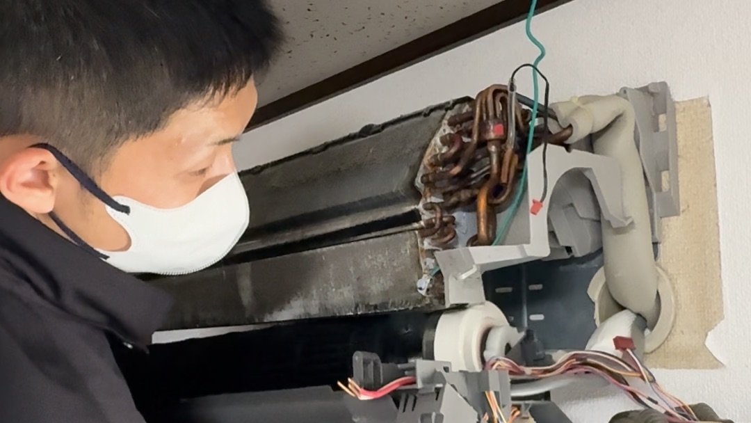 エアコンを完全分解し、熱交換器やドレンパンを露出させた状態で作業するおそうじドットコムの職人